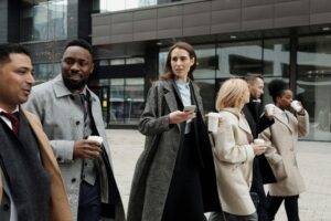 ビジネス街を歩くスーツ姿の男女グループ。会話を交わしながらコーヒーを片手に通勤している様子が写っている