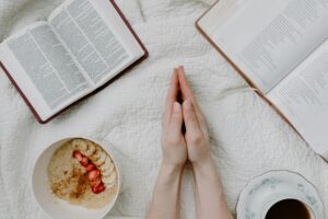 本とコーヒー、果物を前に手を合わせる人。朝の静かなひとときと感謝の時間。